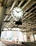 White wall clock with silver edge hanging on roof at train platform.