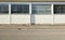 White wall with large windows. Concrete sidewalk and asphalt road in front.