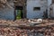 The white walls of an old ruined wooden village house. Broken walls, a ruined roof. Piles of garbage, wooden boards