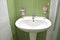 White wash basin, soap container and toothbrush in glass in white green tiled bathroom