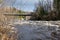 White water in a little river and a bridge crossing, forrest on both sides and a cloudy sky in backgeound