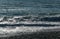 White wave breaking on Sochi Black Sea coast. White spray and foam in the foreground. Emerald blue sea water beyond.