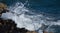 White wave on ocean surface, on a blustery, windy day with rocks in foreground.