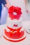 White wedding cake decorated with newlywed first letters, ribbons and red flowers on top