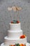 White wedding cake with orange and yellow fondant icing flowers and a succulent plant with three blank wooden bird and heart