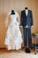 White wedding dress of bride and dark suit of groom on mannequins in room interior