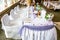 White wedding party table with fancy chairs and a lot of flowers, decorations, beverages and plates with food