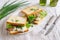 White wheat bread toasted sandwich with pork meat and cheese, salad and sour cream. Chopped chives, bottled olive oil, a knife and