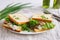 White wheat bread toasted sandwich with pork meat and cheese, salad and sour cream. Chopped chives, bottled olive oil, a knife and