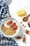 white wheat granola with low-fat yogurt in a white bowl in a composition with a spoon, honeycombs and fig on white wooden