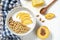 white wheat granola with low-fat yogurt in a white bowl in a composition with a spoon, honeycombs and peach on white wooden