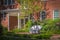 White wicker settee on patio outlide of two story brick house with lots of foliage on bright sunny days with shadows