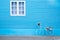 White window on the blue wall with bike shaped flowers pot.