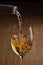 White wine Being Poured into Glass. Stream of wine from bottle and swirls and bubbles in glass. Glass with golden liquid.