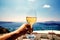 A white wine glass in hand against the backdrop of the Aegean sea and caldera on Santorini island.