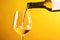 White wine pouring to glass from bottle on yellow background, created using generative ai technology