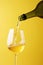White wine pouring to glass from bottle on yellow background, created using generative ai technology