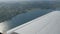 The white wing of a passenger plane against the top view of nature backdrop of a beautiful blue lake, flies over a pond