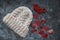 White winter handmade knitted hat with rowan berries and red autumn maple leaves on grey marble background, horizontal