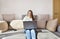 White woman in jeans sitting on the couch with a laptop