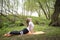 White woman lying on a Mat on the grass in a yoga pose among trees in an outdoor Park