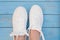 White women`s sneakers on a blue boardwalk background. Clean white sneakers in the center of the frame on the blue wooden floor.