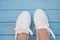 White women`s sneakers on a blue boardwalk background. Clean white sneakers in the center of the frame on the blue wooden floor.