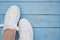 White women`s sneakers on a blue boardwalk background. Clean white sneakers in the left of the frame on the blue wooden floor.