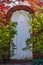 White wooden arched garden gate in autumn in brick wall surrounded by foliage with the sunlight shining around it and through colo