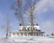 White wooden country house with snowy black roof in winter landscape