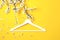 White wooden hanger hanging on the spring flowering branch on yellow background. Spring sale concept discount store shopping empty