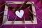 White wooden heart with silk bow across wooden picture frame with lavender on purple textile background close-up. Love concept, St