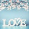 White word LOVE with pastel spring blossom on turquoise blue background, front view. Modern minimal