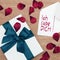 White wrapped gift with a turquoise ribbon and a I-love-you-note in German with a white envelope on a wooden board, surrounded b