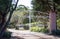 White wrought iron metal driveway entrance gates set in cement brick pillar with residential garden in background