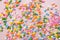 White, yellow, pink, orange, blue and green sprinkles on light pink background with copy space. Colourful edible cake decoration