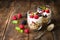 White yogurt with muesli and raspberries in glass bowls on rustic wooden background.