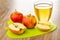 Whole apples, halves of apple and glass with apple juice on cutting board on wooden table