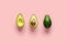 Whole avocado fruit and two halves in a row isolated on pink background