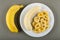 Whole banana, plate with peeled banana and banana chips on gray table. Top view