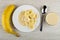 Whole banana, white plate with slices of banana and condensed milk, spoon, bowl with milk on wooden table. Top view