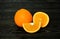 A whole bright juicy ripe beautiful orange, half orange and a piece of orange on a coarse dark wooden background from boards