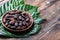 Whole cacao beans in wooden bowl with original fresh leaves on rustic  table close-up