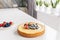 Whole cheesecake with fresh strawberries and blueberries on a white table in white modern kitchen.