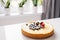 Whole cheesecake with fresh strawberries and blueberries on a white table in white modern kitchen.