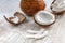 Whole coconut and chopped into chunks and chips on a light white wooden background. Top view