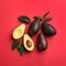 Whole and cut ripe avocadoes with green leaves on red background  flat lay