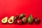 Whole and cut ripe avocadoes on red background, front view, creative. Free space for text. Avocado assortment background, banner,