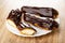 Whole eclairs and halves of eclair with chocolate in plate on wooden table