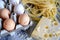 whole eggs in carton beside a heap of spaghetti and a block of cheese